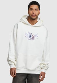 Sudadera blanca de gran tamaño con un bolsillo canguro en la parte frontal, que presenta un gráfico de dos alas y una figura en tonos de púrpura. Textura suave, corte relajado.