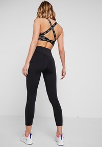 Czarne legginsy sportowe z wysokim stanem, w połączeniu z czarnym stanikiem sportowym z krzyżującymi się ramiączkami i białymi akcentami logo.