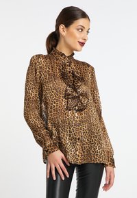 Blusa con stampa leopardata, colletto alto arruffato, maniche lunghe e chiusura a bottoni. Realizzata in tessuto leggero, presenta dettagli neri.
