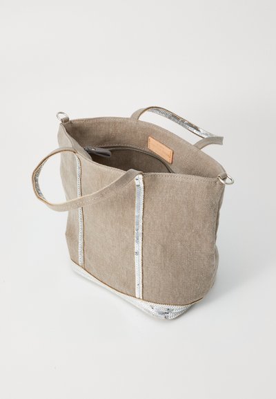 Tote bag en tissu beige avec des accents de zip argentés, des poignées doubles et une poche intérieure zippée. Texture douce avec une forme structurée.
