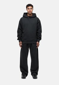 Zwarte oversized hoodie met een voorzak en bijpassende wijde sweatpants, gemaakt van zachte stof met een gladde textuur.