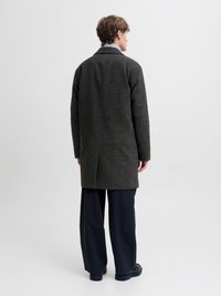 Mørk ullblandingsfrakk med skreddersydd passform, notched revers og enkel splitt, kombinert med vide svarte bukser og solide svarte sko.