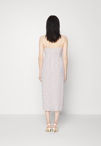 Blomsterprintet, ærmeløs midi-kjole med et tætsiddende skørt, elastiske samlinger og et glat stof i pastelfarver, parret med beige hæle.