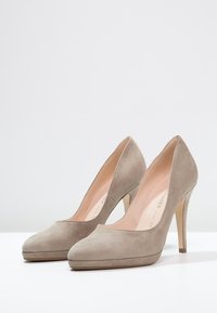 Pair of beige suede high-heeled pumps with pointed toes and platform soles placed on a white surface against a plain background.