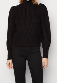 Maglione a collo alto nero con texture a coste, maniche a sbuffo e silhouette aderente. Presenta un piccolo accento decorativo sulla spalla.