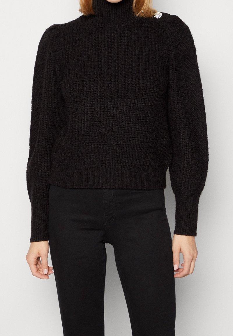 Maglione a collo alto nero con texture a coste, maniche a sbuffo e silhouette aderente. Presenta un piccolo accento decorativo sulla spalla.
