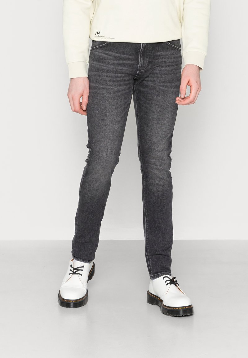 Slim fit grå jeans i denim med subtila blekningar, matchade med vita skor med svarta snören och en kraftig sula. Minimalistisk design.