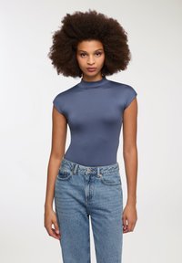 Granatowy, dopasowany bodysuit z wysokim dekoltem i krótkimi rękawami, połączony z jasnoniebieskimi jeansami z wysokim stanem z zapięciem na guzik i zamek.