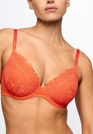 Woman wearing orange lace bra with floral patterns and adjustable straps, shown from shoulders to midriff against plain background.