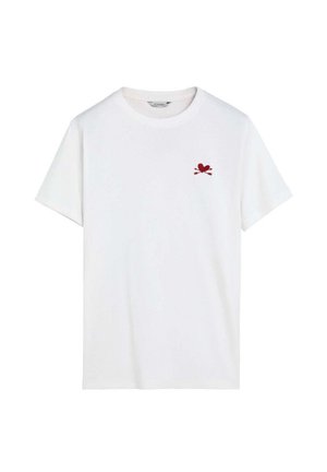 Camiseta blanca de manga corta con cuello redondo y pequeño emblema de corazón rojo y flechas cruzadas en el pecho izquierdo.