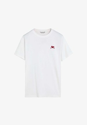 Camiseta blanca de manga corta con cuello redondo y pequeño emblema de corazón rojo y flechas cruzadas en el pecho izquierdo.