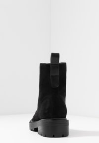 Botines de ante negro con una suela de goma gruesa y una tira en la parte trasera para facilitar el calce. El diseño presenta una textura suave y sutiles detalles de costura.