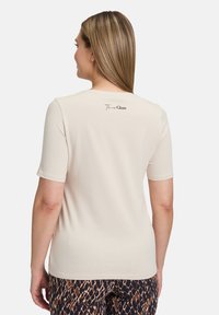 T-shirt beige à manches courtes avec un col rond, portant l'inscription "The New Glam" au dos, fabriqué en tissu doux et léger.
