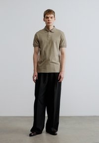 Polo bege com mangas curtas, combinado com calças pretas largas. Design simples da gola, textura suave e detalhes mínimos.