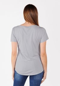 Camiseta gris de manga corta con un escote relajado, textura suave y dobladillo curvado, combinada con jeans de mezclilla azules.