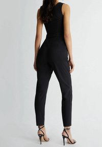 Mono negro ajustado con un diseño sin mangas, piernas entalladas y una textura suave. Combinado con sandalias negras de tacón alto.