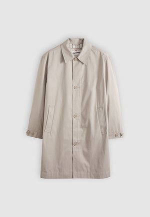 Bež dolg bombažen plašč s sponko za zapenjanje na gumbe, koničastim ovratnikom, dvema žepoma spredaj in sproščenim krojem. Na rokavih ima gumbe kot okras.