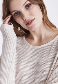 Helles Beige, gestrickter Pullover mit lockerer Passform, weitem Ausschnitt und langen Ärmeln; zeichnet sich durch eine gerippte Textur und ein dezentes offenes Gewebedesign aus.