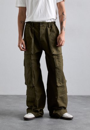 Pantalons cargo en vert olive foncé, en coton, dotés de plusieurs poches, d'une taille élastique et d'une coupe ample. Associés à des baskets blanches.