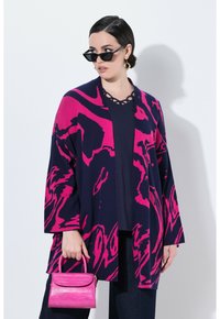 Námořnický a růžový vzorovaný cardigan s tříčtvrtečními rukávy, doplněný malou růžovou kabelkou a námořnickým topem, nošený s tmavými džíny.