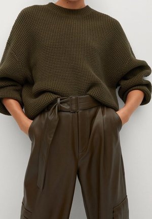 Personne portant un pull en maille texturée vert olive foncé avec les manches retroussées, associé à un pantalon en cuir marron taille haute avec ceinture.