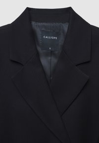 Blazer nero con colletto a risvolto, texture liscia e fodera in satin. Presenta un'etichetta con la scritta "CALLIOPE" e la taglia "S".
