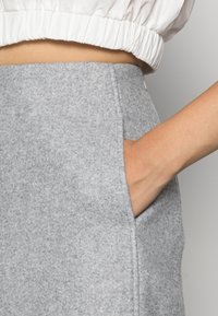 Grå filtkjol med en sidficka, som har en ren design och mjuk textur, tillsammans med en rynkad, vit kort topp.