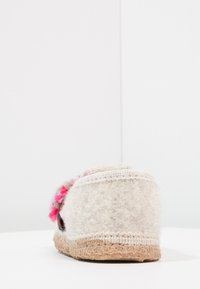 Chausson en feutre avec un extérieur texturé beige et un accent de pompon coloré. Semelle en caoutchouc beige avec des détails de couture.