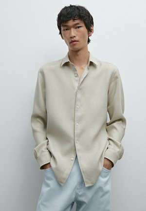 Light beige long-sleeve shirt in a woven fabric, featuring a button-down front, relaxed fit, and pointed collar, paired with light blue pants.