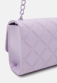 Lilac crossbody bag made of textured, smooth faux leather featuring diamond patterns and chain strap detail. Edges are stitched in white.