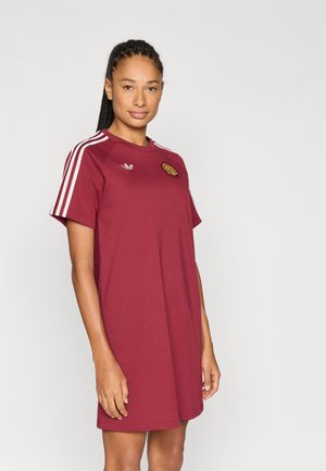 Dieprode sportjurk met witte drie-strepen accenten op de schouders, ronde halslijn en geborduurd logo op de borst. Korte mouwen, gladde textuur.