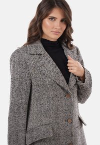 Blazer con motivo a pied de poule in grigio e bianco, con grandi bottoni, rever a lancia e tessuto strutturato. Tasche su entrambi i lati.