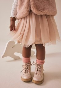 Jupe en tulle rose superposée sur un haut blanc, associée à des bottes à lacets rose clair brillantes et à des chaussettes en tricot rose doux.