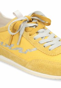 Baskets en daim et tissu jaune avec lacets blancs et jaunes, semelle blanche et détail du logo argenté sur le côté.