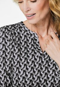 Blusa a fantasia bianca e nera con un design geometrico, dotata di scollatura a V e dettagli plissettati sulle spalle. Tessuto morbido.