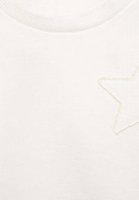 Valkoinen neulepusero, jossa on pehmeä rakenne, ja vasemmassa rinnassa kevytbeige tähti brodeerattuna. Pyöreä ribbaus kaula-aukossa.