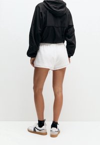 Veste noire courte, short blanc texturé avec une taille élastique, et chaussures blanches avec des accents noirs et une semelle beige.