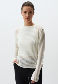 Pull en tricot blanc avec un design texturé en mailles ouvertes, des manches longues et un col rond. Accentué par un ourlet et des poignets côtelés.