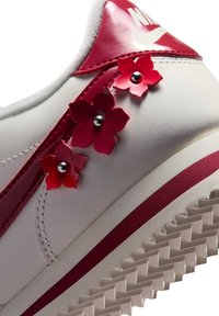 White Nike sneaker with red accents and three decorative red flowers with metallic centers on the side near the heel.
