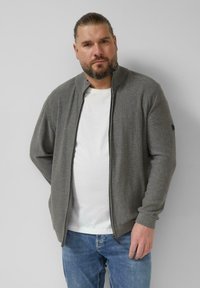 Grauer Reißverschluss-Cardigan aus weichem Material, mit einem gerippten Kragen und Bündchen. Getragen über einem weißen T-Shirt mit blauen Jeans.