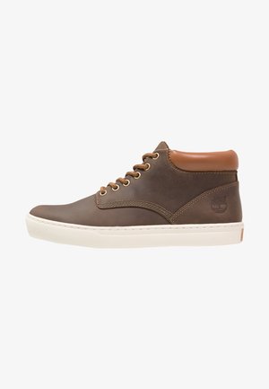 Baskets montantes en cuir marron avec col matelassé beige, lacets marron, semelle épaisse blanche et logo embossé sur le côté du talon.