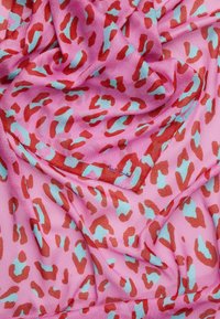 Tissu rose clair présentant un motif léopard en rouge et turquoise. La texture est douce et lisse, adaptée aux accessoires.