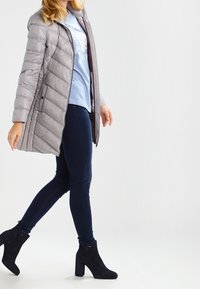 Lys grå pufferjakke med diagonal syning, parret med mørkeblå skinny jeans og sorte ankelstøvler. Jakken har en lynlåslukning.