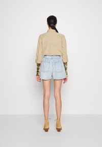 Béžová košile na knoflíky, světlé modré džíny šortky, hnědé kotníkové boty s blokovými podpatky. Hladká tkanina, volný střih a dvě zadní kapsy na šortkách.