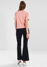 Jasnoróżowa bluzka z krótkim rękawem zestawiona z granatowymi spódnicami dzwonami. Gładki materiał o klasycznym kroju, z przeszyciem na plecach. Białe buty na obcasie w kształcie bloku.