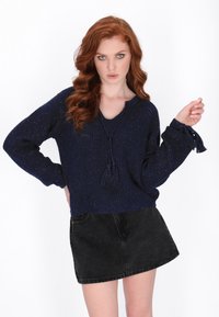 Granatowy sweter dzianinowy z dekoltem w kształcie V, teksturowaną powierzchnią i detalem w postaci chwosta; zestawiony z czarną spódnicą dżinsową.