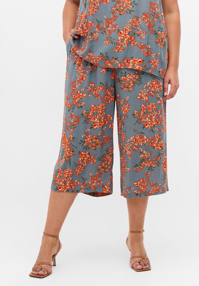 Ensemble haut floral et culottes, avec un fond gris orné de fleurs orange. Coupe ample, tissu léger, et pantalons longueur cheville.