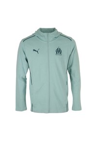 Giacca con zip di colore azzurro chiaro realizzata in materiale morbido, con cappuccio, logo Puma nero ed emblema del club di Marsiglia sul petto.