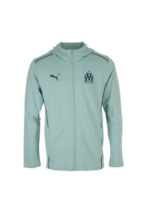 Veste zippée bleu clair en matériau doux, dotée d'une capuche, avec un logo Puma noir et un emblème du club de Marseille sur la poitrine.