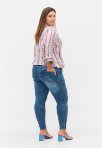 Blusa de manga larga con un patrón a rayas en crema, azul y rosa, combinada con vaqueros ajustados azules con detalles desgastados y bolsillos.
